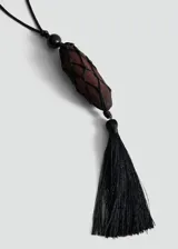 Collar largo ajustable con cordón negro, cuenta con un dije central de madera revestido en red negra y una borla colgante de flecos en la parte inferior.
