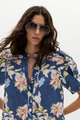 Vestido corto azul de lino con estampado floral en tonos rosados, beige y celestes, cuello mao con escote en V, mangas cortas abullonadas, botones frontales ocultos y volado en el ruedo.