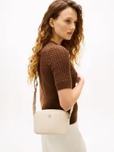 Cartera bandolera de poliuretano color beige, de diseño estructurado con compartimento principal con cierre, bolsillo interior y correa ajustable. Cuenta con el logo metalizado de la marca en el frente y detalles dorados.