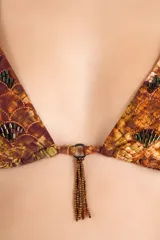 Top de bikini triangular con estampado de efecto piel de serpiente en tonos marrones y dorados, con delicados bordados de cuentas oscuras y detalle de flecos metálicos colgando en el centro.