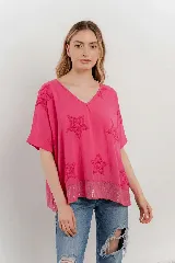 Blusa fucsia de algodón, con escote en V, mangas cortas y silueta amplia. Presenta estrellas bordadas en relieve y un detalle de lentejuelas en el dobladillo inferior.