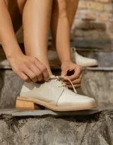 Zapato acordonado de cuero vacuno color crema, con diseño de textura combinada que incluye paneles lisos y paneles con efecto croco. Presenta una horma cuadrada, cordones al tono y una suela de madera con base de goma.