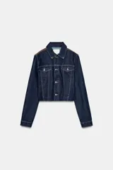 Cazadora de corte cropped confeccionada en tejido denim azul oscuro, con cuello solapa, cierre frontal de botones metálicos y bolsillos con solapa en el pecho. Presenta detalles de aplicación en piel a contraste en la zona de los hombros.