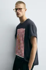 Camiseta azul marino de corte relaxed fit, cuello redondo y manga corta. Presenta un parche rectangular estampado con rayas horizontales rojas y blancas, y un dibujo de una langosta en el centro.