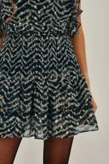 Falda corta con estampado de zigzag en tonos azul marino y beige, con detalles dorados. Presenta un canesú fruncido a la cintura y volados en el ruedo. Tiene escote en V con detalle de encaje en el borde.