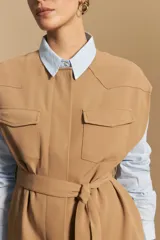 Chaleco negro de corte estructurado con cuello redondo, cierre frontal oculto y lazo ajustable en la cintura. Presenta dos bolsillos frontales con solapa y diseño de hombros caídos.