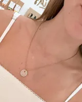 Collar de cadena fina de acero en tono dorado con dije circular central de resina rodeado por una hilera de strass brillantes.