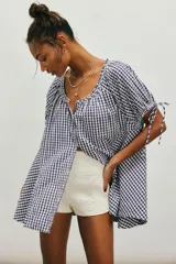 Túnica de algodón liviano con estampado de cuadros vichy en color azul marino y blanco. Presenta caída amplia y largo extendido, escote redondo con botonadura frontal y mangas cortas abullonadas con lazos ajustables.