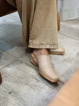 Zuecos color beige con diseño bordado en el empeine, taco de madera y punta cuadrada.