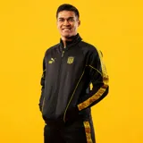 Campera deportiva Puma modelo CAP King Jacket, color negro con detalles en amarillo. Posee cierre frontal, cuello alto y franjas laterales estampadas en las mangas.