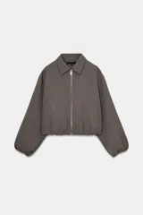 Chaqueta de corte corto y diseño abullonado en color marrón oscuro, con cuello solapa, mangas largas con puños elásticos y cierre frontal con cremallera metálica. Cuenta con bolsillos delanteros de doble vivo.