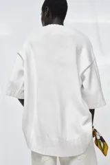 Jersey amplio de punto color blanco, con cuello redondo, manga corta y bajo asimétrico.