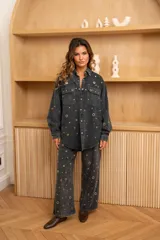 Camisa oversize de algodón color gris oscuro, con cuello camisero, cierre frontal con botones a presión, dos bolsillos con solapa en el pecho y ojales metálicos dorados y plateados.