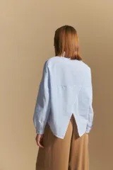 Camisa de manga larga a rayas verticales blancas y azules, con cuello camisero, cartera frontal con botones y calce relajado.