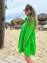 Vestido camisero corto color verde manzana, con cuello camisero, mangas largas con puños abotonados, cierre frontal con botones a tono y falda fruncida con volantes.