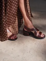 Sandalias de cuero color marrón con tiras anchas cruzadas y hebilla metálica decorativa en forma de estribo. Presentan taco cuadrado de altura media y suela de goma.