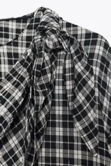 Camisa de manga larga con estampado a cuadros en blanco y negro. Presenta un cuello redondo y un pañuelo multiposición que cae en un drapeado asimétrico sobre el frente.