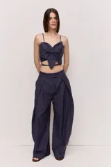 Pantalón azul marino de tiro alto con cintura ancha y pliegues frontales que aportan volumen y una caída suelta y fluida, con diseño envolvente en la cadera y bolsillos laterales.