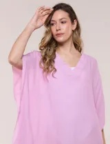 Vestido playero tipo túnica de corte holgado color rosado, confeccionado en tejido semi transparente con textura sutilmente arrugada. Cuenta con escote en V pronunciado, mangas estilo kimono de caída fluida y aberturas laterales en el ruedo irregular.