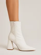 Bota corta blanca de cuero sintético, con punta fina, cierre lateral y taco geométrico.