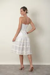 Vestido midi strapless color marfil, con diseño de paneles horizontales que combinan encaje y detalles de flecos. Presenta una falda con vuelo y movimiento.