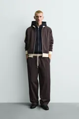 Sudadera de corte relajado en color azul marino con cuello alto y cierre frontal de cremallera. Presenta bandas laterales en color crema a contraste que recorren las mangas, puños y bajo en tejido rib, y bolsillos laterales de vivo.