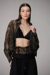 Camisa negra de encaje semitransparente con diseño floral, cuello camisero y mangas largas.