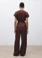 Pantalón de tiro medio en tejido satinado con efecto arrugado y diseño recto. Cuenta con bolsillos laterales, pinzas delanteras y cierre oculto con botón, gancho y cremallera.