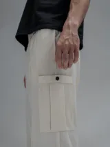 Pantalón cargo de corte oversize confeccionado en microfibra elastizada color beige. Presenta cintura elástica, bolsillos laterales y un bolsillo cargo con cierre de broche a presión. Incluye un sistema de elásticos con tancas en los tobillos para ajustar la apertura.
