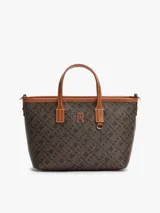 Cartera tote Tommy Hilfiger de acabado texturizado con estampado integral del monograma TH en tonos marrón y negro. Cuenta con dos asas superiores de cuero sintético tostado, bandolera extraíble, cierre de cremallera y herrajes metálicos dorados. Incluye una insignia del monograma en el frente y un detalle de anilla en D.