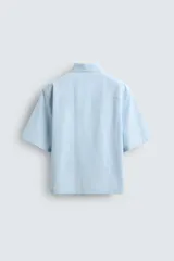 Camisa de corte relajado confeccionada en tejido de mezcla de algodón, con estampado de rayas verticales en tonos azul y blanco. Presenta cuello solapa, manga corta y cierre frontal con botones. Incluye un detalle bordado a contraste en el pecho.