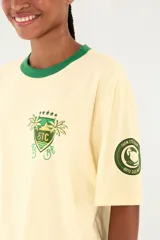 Camiseta Ipanema de manga corta en color amarillo pastel, con cuello redondo en contraste de color verde oscuro. Presenta un pequeño estampado en el pecho con diseño de escudo y palmeras.