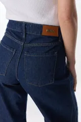 Pantalón de pierna ancha con acabado brillante, confeccionado en lino. Presenta un diseño de tiro medio con cierre de botón y cremallera, bolsillos traseros y etiqueta de marca en la cintura.