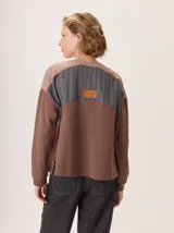 Buzo de algodón color beige con cuello redondo y cierre frontal parcial de cuatro botones. Presenta mangas largas con puños elastizados, inserciones de lana en los hombros y detalles de costuras a la vista.