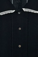 Chaqueta de punto de manga corta con cuello polo y cierre frontal de botones, en color negro con detalles de puntilla blanca en el cuello y los puños.