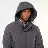 Campera acolchada de corte recto en color gris, con capucha ajustable, cierre frontal de cremallera y botones a presión, y bolsillos laterales.