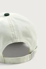 Gorra de seis paneles con efecto lavado, de color blanco crudo con visera en verde militar. Presenta un bordado frontal contrastante con texto en negro y una estrella roja.