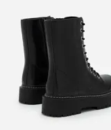 Bota tipo coturno de caña media, confeccionada en poliuretano color negro, con cierre frontal de cordones, cremallera lateral y suela track robusta.