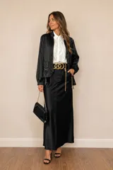 Campera tipo bomber color negro, confeccionada en tejido satinado. Presenta cierre frontal metálico, bolsillos laterales con hebillas decorativas doradas y puños elásticos.