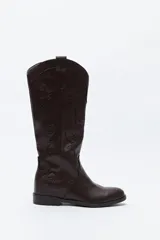 Bota de caña alta estilo western confeccionada en cuero sintético, con bordados decorativos en relieve a lo largo de la caña y puntera afinada.