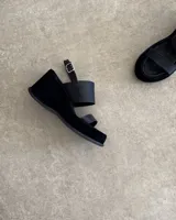 Sandalias de cuero vacuno color negro, con taco de cuña y tira ancha sobre el empeine. Ajuste con hebilla al tobillo.