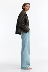 Jean de denim de algodón rígido color celeste claro, de tiro alto y corte recto holgado. Presenta bolsillos al bies y pliegues marcados adelante y atrás.