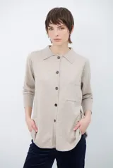 Cardigan de punto color beige, con cuello camisero, cierre frontal de botones y bolsillo aplicado en el pecho. Presenta mangas largas con puños acanalados y un corte recto y holgado.
