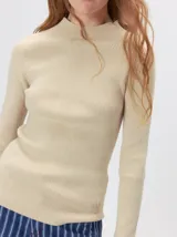 Remera de cuello alto tipo polera, confeccionada en tela rib con textura acanalada y ajuste al cuerpo. Presenta mangas largas y un pequeño bordado distintivo en la parte inferior.