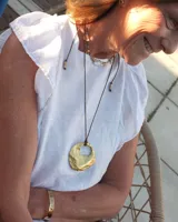 Collar artesanal con dije de bronce macizo en forma orgánica irregular, similar a una concha marina, suspendido de un cordón de seda natural negro. El diseño permite diversas formas de uso, ya sea ajustado al cuello o largo.