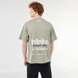 Remera de algodón verde militar, de corte holgado y manga corta, con cuello redondo y estampado frontal con texto en blanco y negro.