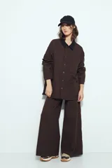 Sobrecamisa tipo Barn Jacket color marrón oscuro, de algodón con elastano, silueta relajada y estructura firme. Presenta cierre frontal con botones metálicos, cuello negro, bolsillos aplicados y pespuntes visibles.