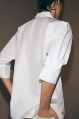 Camisa de algodón con cuello redondo y escote en pico, mangas tres cuartos con puños y bajo asimétrico redondeado.