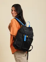 Mochila marrón con detalles en violeta. Tiene un bolsillo frontal superior con cierre, un bolsillo lateral de red y el logo de Rusty Worldwide estampado en naranja.