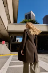 Abrigo de paño color beige con cuello solapa, manga larga con hombreras y cierre frontal con botones. Presenta bolsillos delanteros de doble vivo y abertura en la espalda.